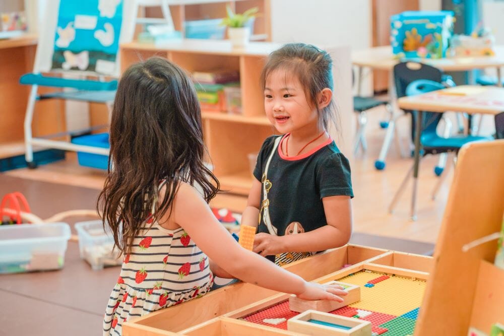Two children engage in conversation while playing with an activity inside a child care classroom.
